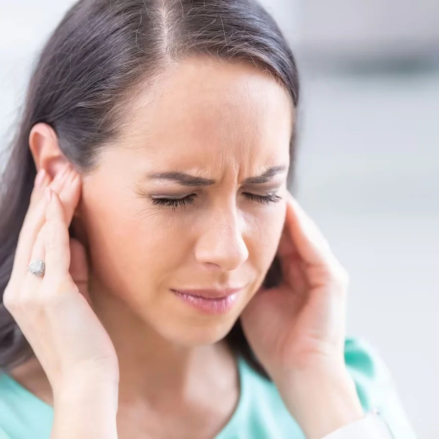 Woman holding her ear, illustrating the causes of tinnitus